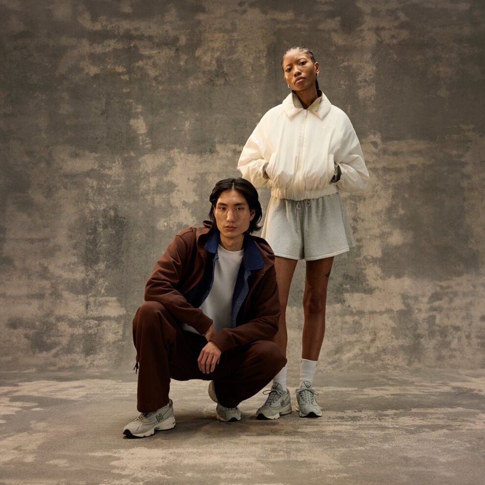 Two people posing indoors against a textured backdrop, wearing casual athletic outfits and sneakers. 